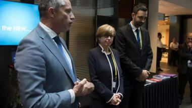Das Bild zeigt drei Personen (in der Mitte Catherine De Bolle) auf einer Pressekonferenz vor einer Leinwand mit den Worten "And the NEW...".