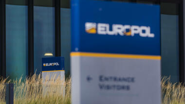 Das Bild zeigt einen Ausschnitt der Zentrale von Europol, im Vordergrund verschwommen ein Schild mit der Aufschrift "Europol".