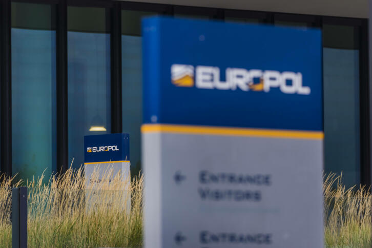 Das Bild zeigt einen Ausschnitt der Zentrale von Europol, im Vordergrund verschwommen ein Schild mit der Aufschrift "Europol".