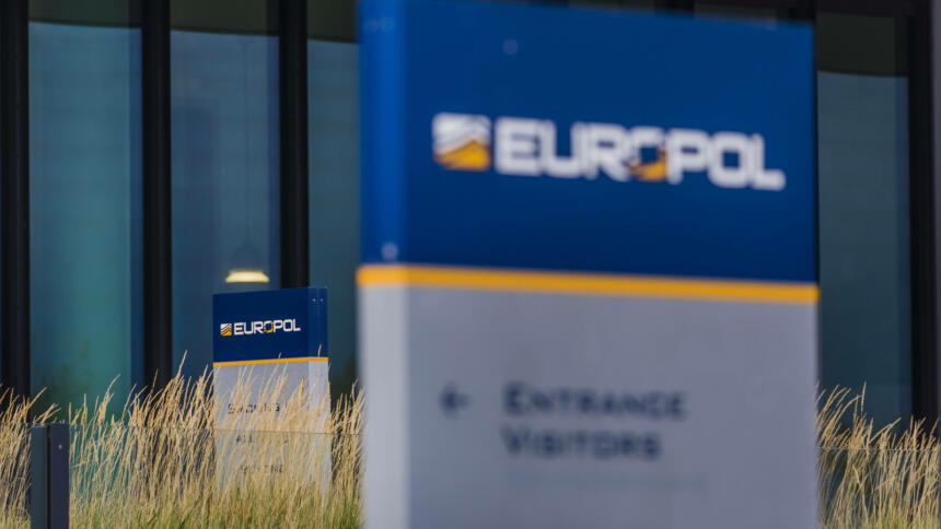 Das Bild zeigt einen Ausschnitt der Zentrale von Europol, im Vordergrund verschwommen ein Schild mit der Aufschrift "Europol".