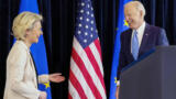 Eine Frau und ein Mann, lachend, vor Fahnen der USA und EU