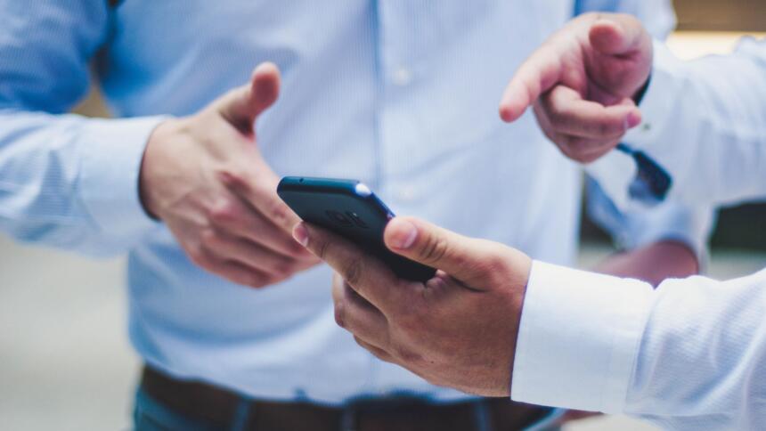 Zwei Menschen in Business-Hemden gestikulieren mit Smartphone in der Hand