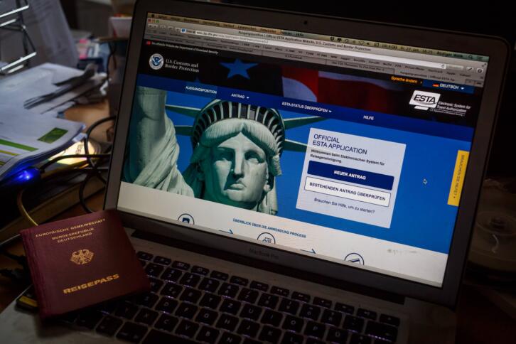 Ein Monitor, auf dem die ESTA-Seite aufgerufen ist. Daneben ein Reisepass.