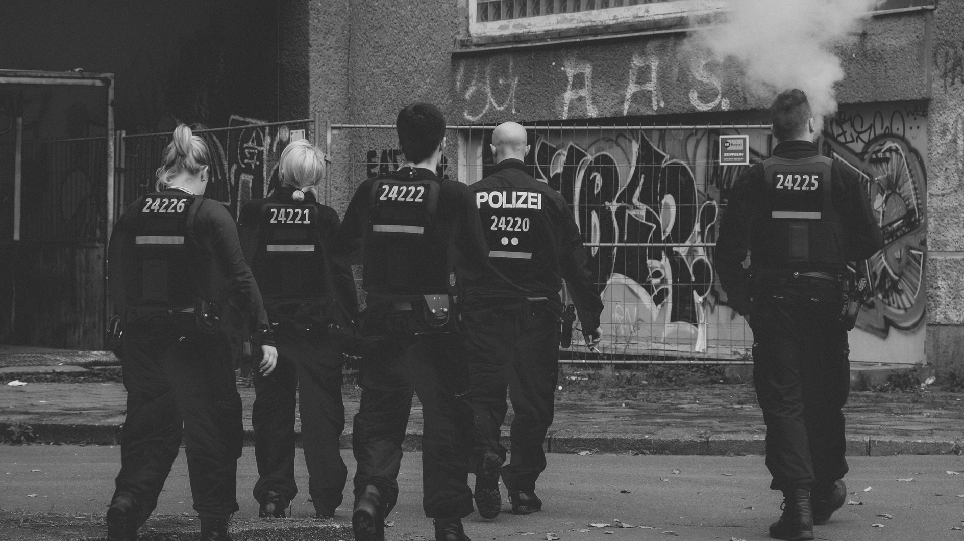 Eine Gruppe von Polizist:innen laufen auf ein Haus zu.