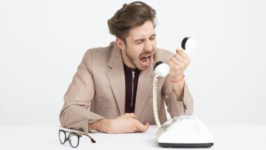 Ein junger Mann mit braunen Haaren brüllt in ein weißes, altmodisches Telefon