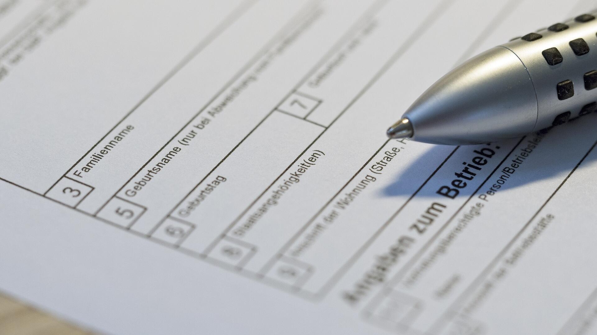 Ein Kugelschreiber liegt auf einem Antragsbogen. Die Felder für Familienname, Geburtsname und Geburtsdatum sind zu sehen.