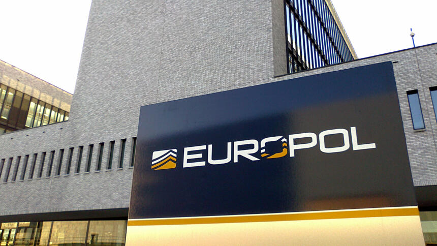 Das Bild zeigt das graue Europol-Gebäude mit einem Emblem der Agentur im Vordergrund.