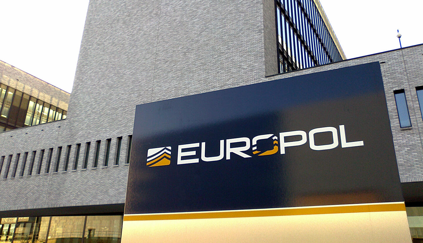 Das Bild zeigt das graue Europol-Gebäude mit einem Emblem der Agentur im Vordergrund.