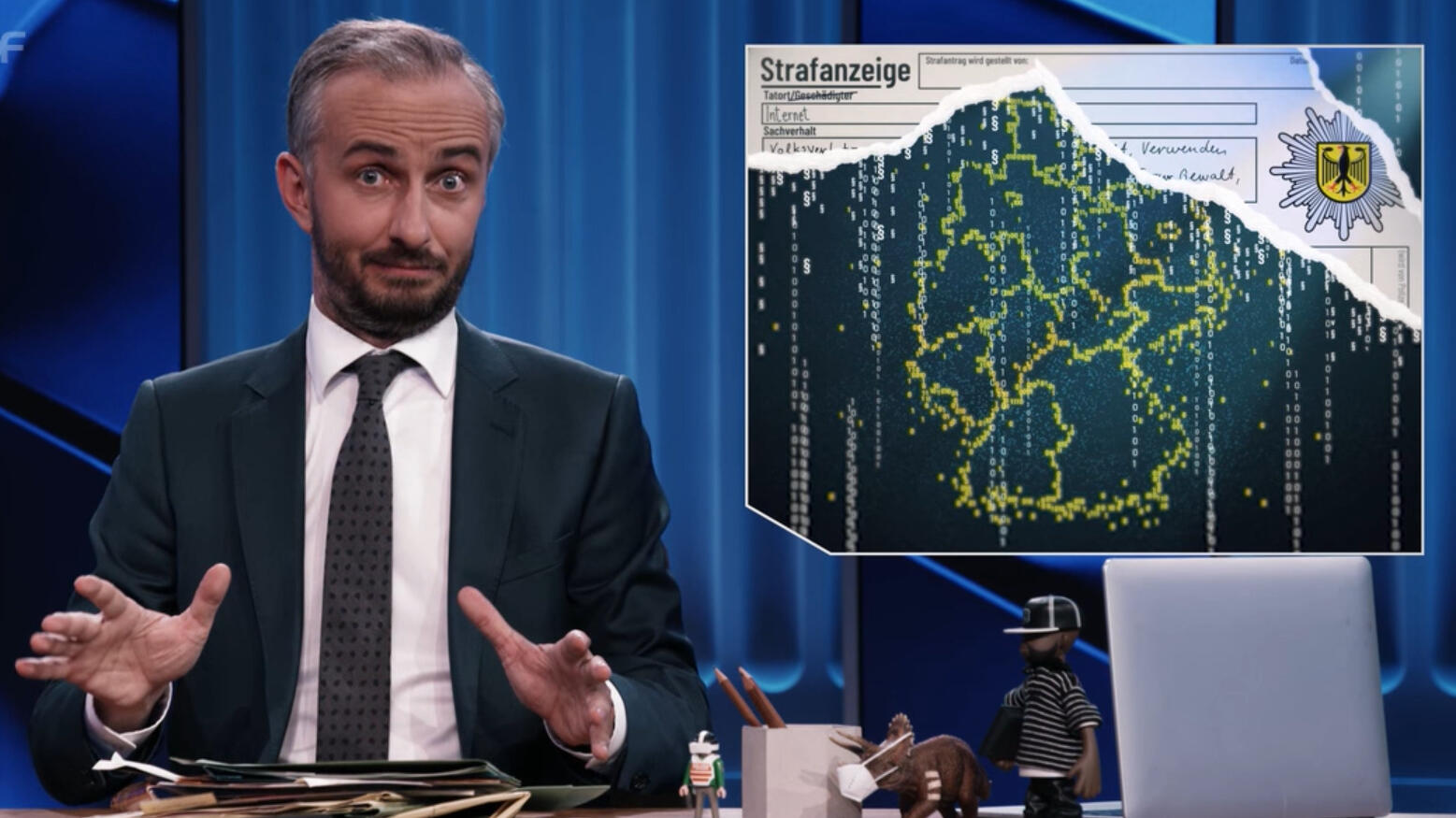 jan böhmermann sitzt an einem tisch. neben ihm ist eine deutschlandkarte eingeblendet mit ländergrenzen