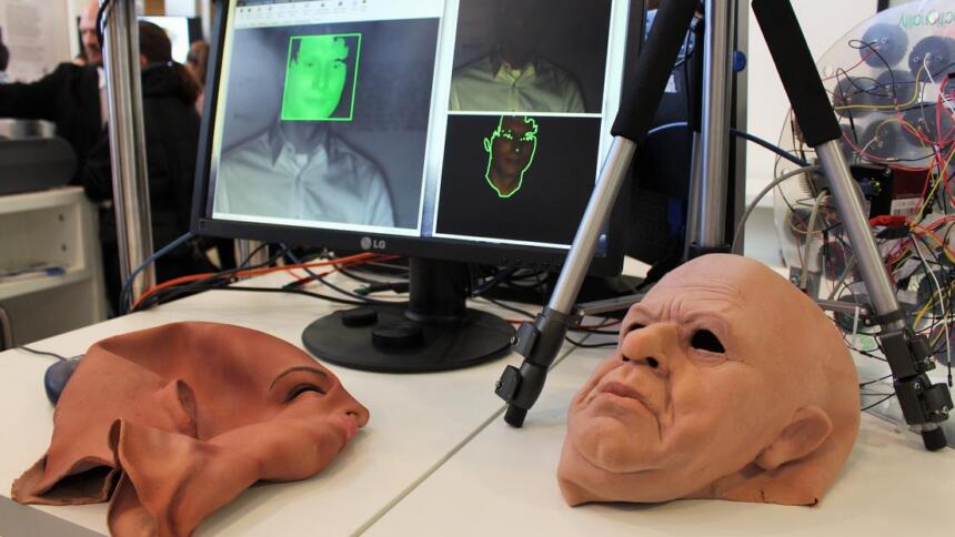 Vor einem Monitor, auf dem ein Gesichtserkennungsprogramm geöffnet ist, liegen zwei Gesichtsmasken.