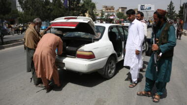 Die Taliban in Afghanistan durchsuchen den Kofferraum eines weißen Autos, das auf der Straße steht.