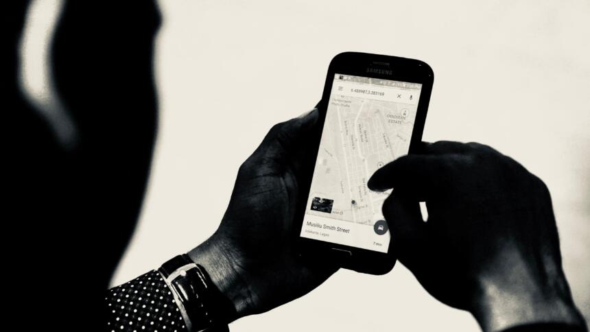 Ein Mann hält ein Smartphone in den Händen. Auf dem Smartphone ist eine Landkart zu sehen. Mit der rechten Hand bedient die Person das Smartphone.