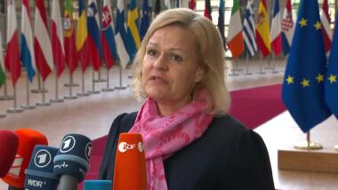 Nancy Faeser spricht in Mikrofone, im Hintergrund Fahnen von EU-Mitgliedstaaten.