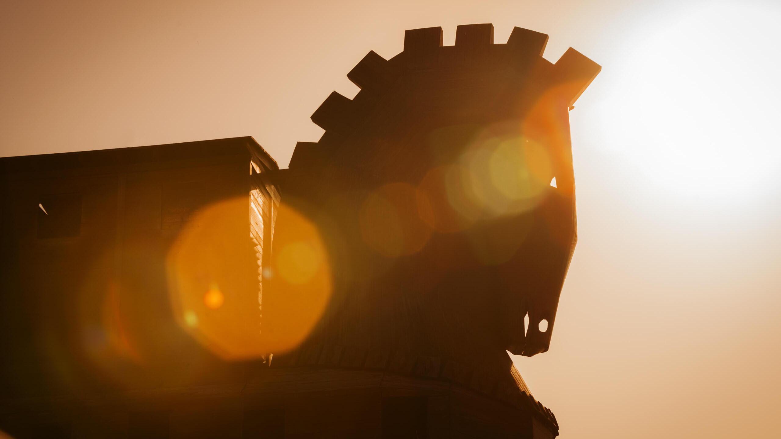 ein trojanisches Pferd aus Holz sieht man hier gegen das Sonnenlicht. Dabei sieht der Kopf des Pferdes bedrohlich aus.