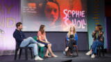vier Personen sitzen auf einer Bühne und diskutieren miteinander. Im Hintergrund ist auf einer Leinwand, das Gesicht der Schauspielerin von Sophie Scholl zu sehen.
