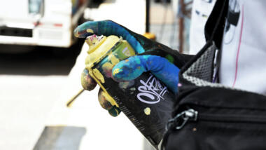 Das Bild zeigt eine Hand, die einen Handschuh trägt und eine Spraydose für Farbe hält.