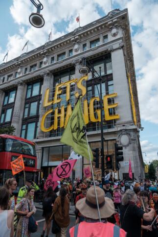 Eine Demonstration von Extinction Rebellion vor einem Gebäude auf dem der Schriftzug "Let's Change" angebracht ist.