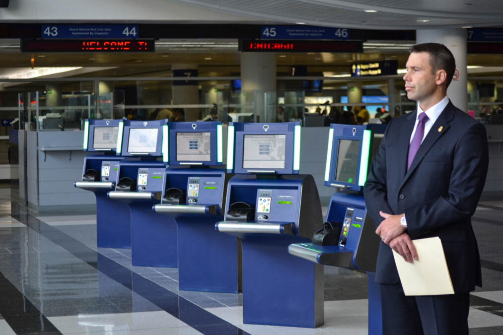 Ein ernst drein blickender US-Beamter steht vor einer Reihe von Passlesegeräten.