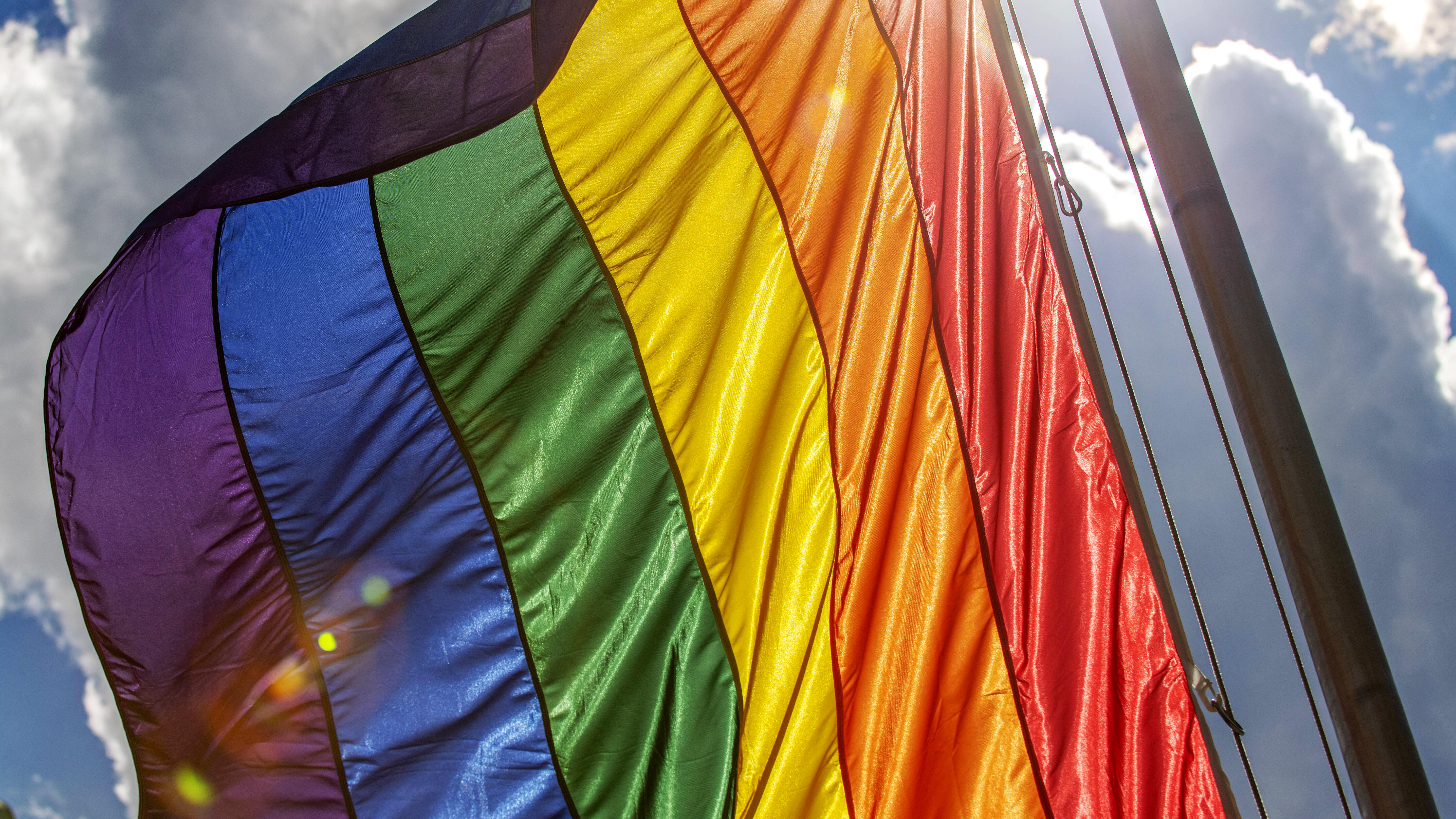Regenbogenflagge vor Wolkenhimmel im Sonnenschein