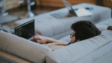 Ein Mann liegt mit Laptop auf dem Sofa