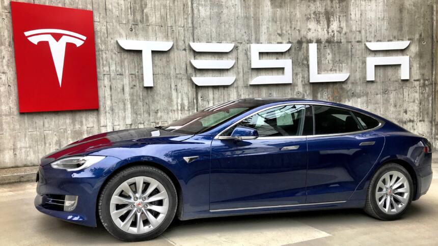 Ein Tesla-Auto steht vor einer Wand mit großer Aufschrift "TESLA"