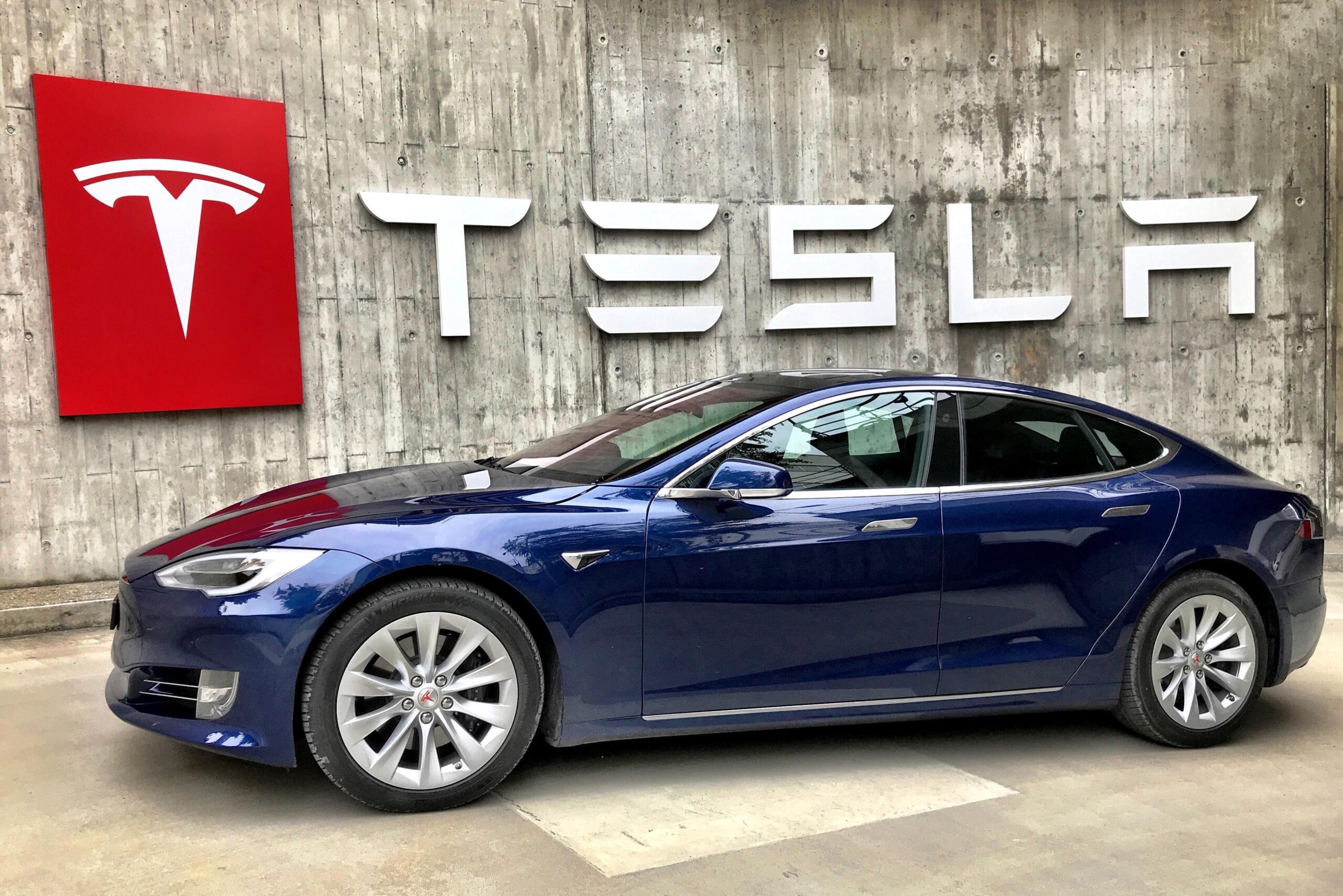 Ein Tesla-Auto steht vor einer Wand mit großer Aufschrift "TESLA"