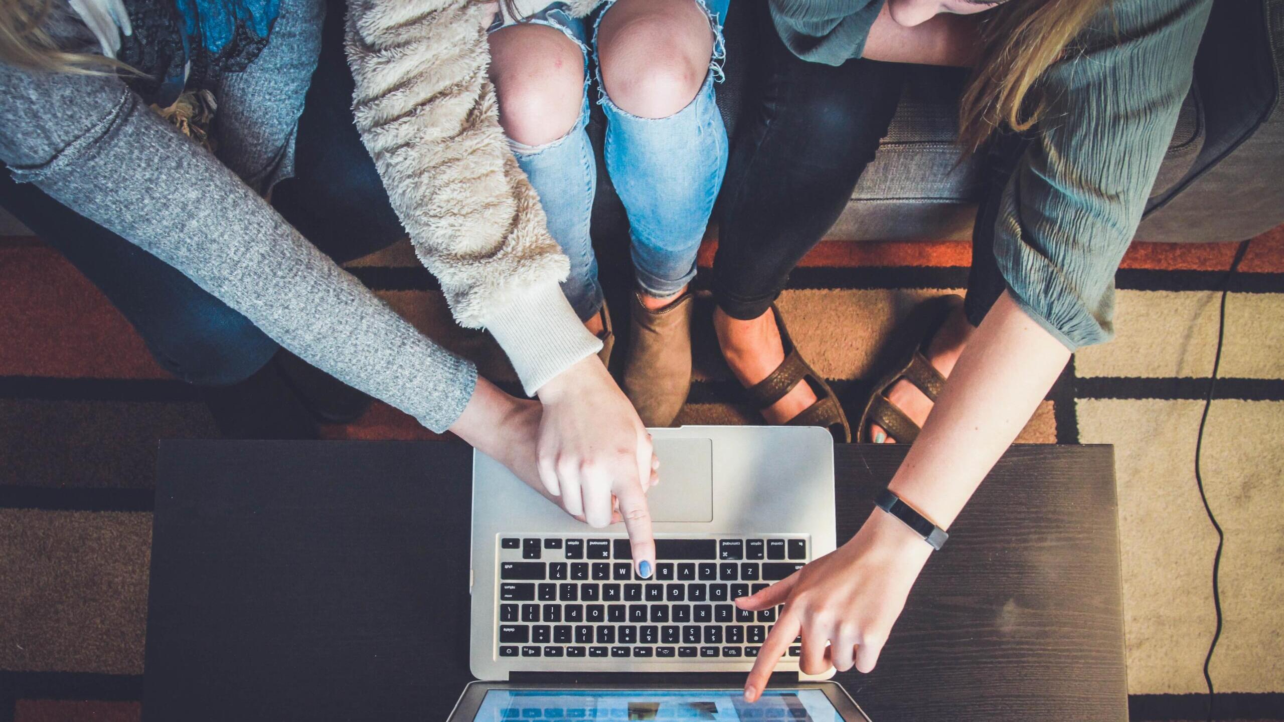 Foto von oben, wie mehrere Menschen auf einen Laptop-Bildschirm zeigen