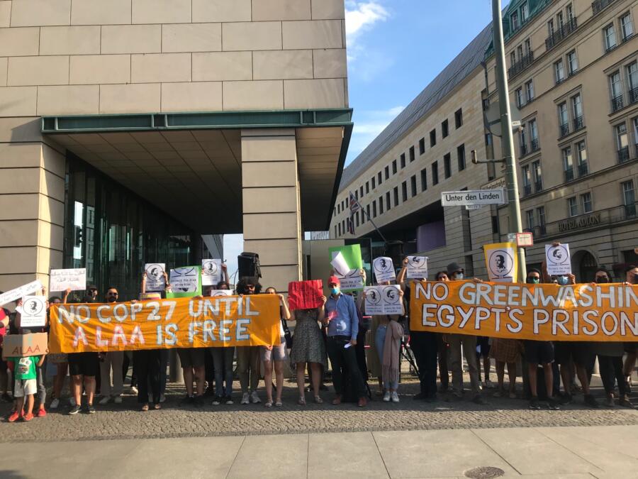 Zwei Dutzend Personen halten ein Transparent "No Greenwashing Egypt's Prisons No Cop27 Until Alaa Is Free" an der Kreuzung der Straße Unter den Linden/ Wilhelmstraße.