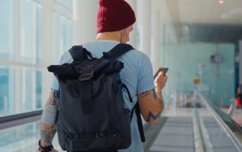 Ein von hinten aufgenommener Reisender auf einem Laufband, der auf sein Handy schaut.