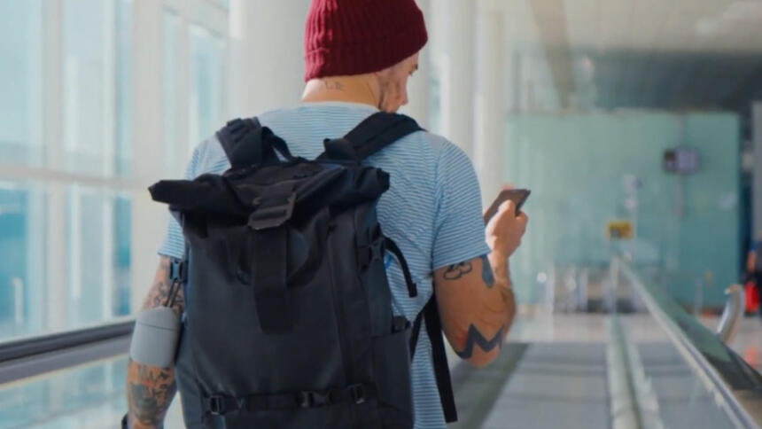 Ein von hinten aufgenommener Reisender auf einem Laufband, der auf sein Handy schaut.