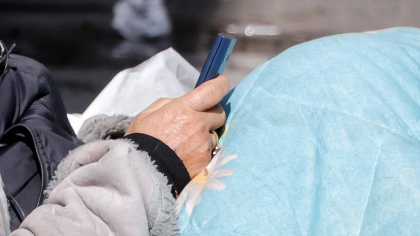Obdachlose Person mit Schlafsack mit Handy in der Hand