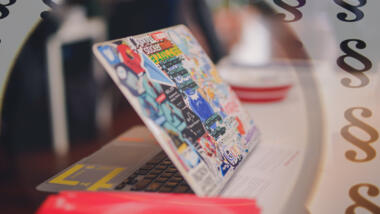 Ein Laptop mit Stickern beklebt, im Hintergrund Paragrafen