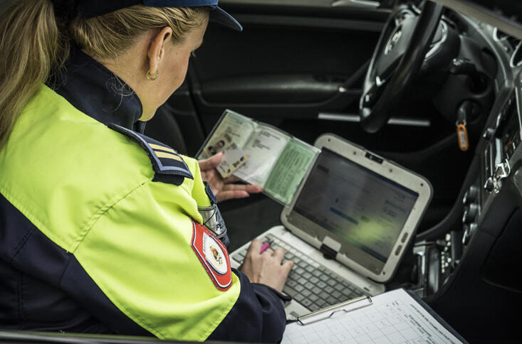 Eine Polizistin mit Ausweisdokumenten und Laptob auf einem Beifahrersitz.