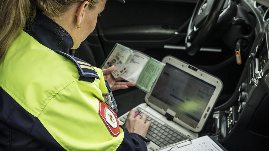 Eine Polizistin mit Ausweisdokumenten und Laptob auf einem Beifahrersitz.