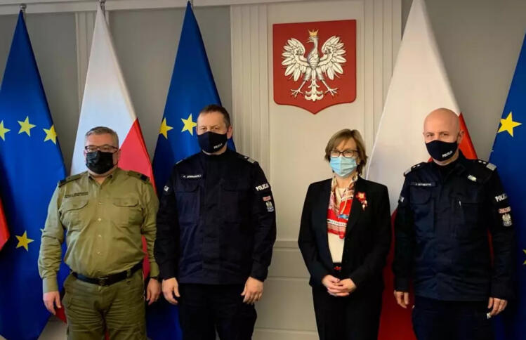 Die EUropol-Chefin zwischen drei Männern in Uniformen, im Hintergrund das polnische Wappen an der Wand.
