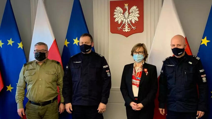 Die EUropol-Chefin zwischen drei Männern in Uniformen, im Hintergrund das polnische Wappen an der Wand.