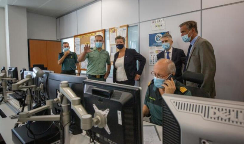 Ein Mann vor einem Monitor, im Hintergrund Johansson mit einem Polizisten, umringt von drei Männern, alle mit Masken.