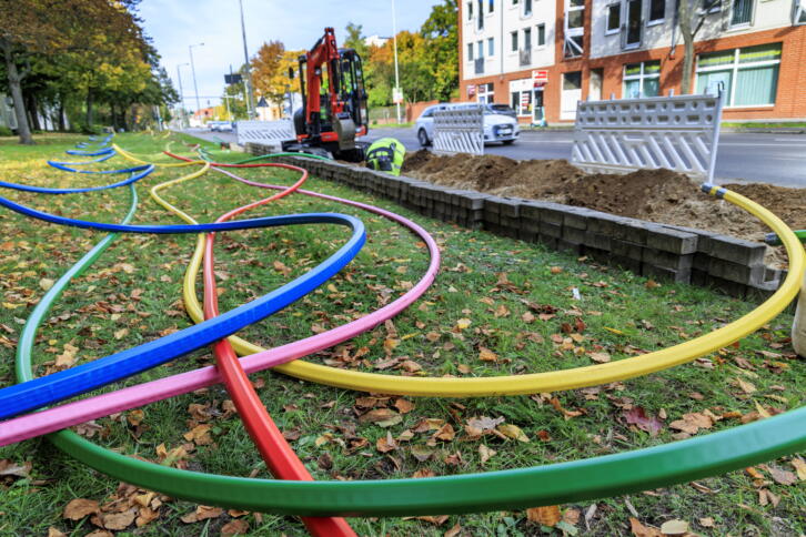 Bunte Leitungen für den Glasfaserbau auf einer Wiese.