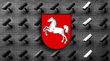 Eine Wand voller Überwachungskameras, davor das Wappen von Niedersachsen mit einem weißen Pferd auf rotem Grund