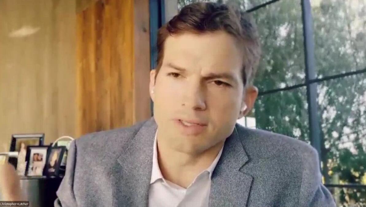 Ashton Kutcher vor brauner Holzwand.