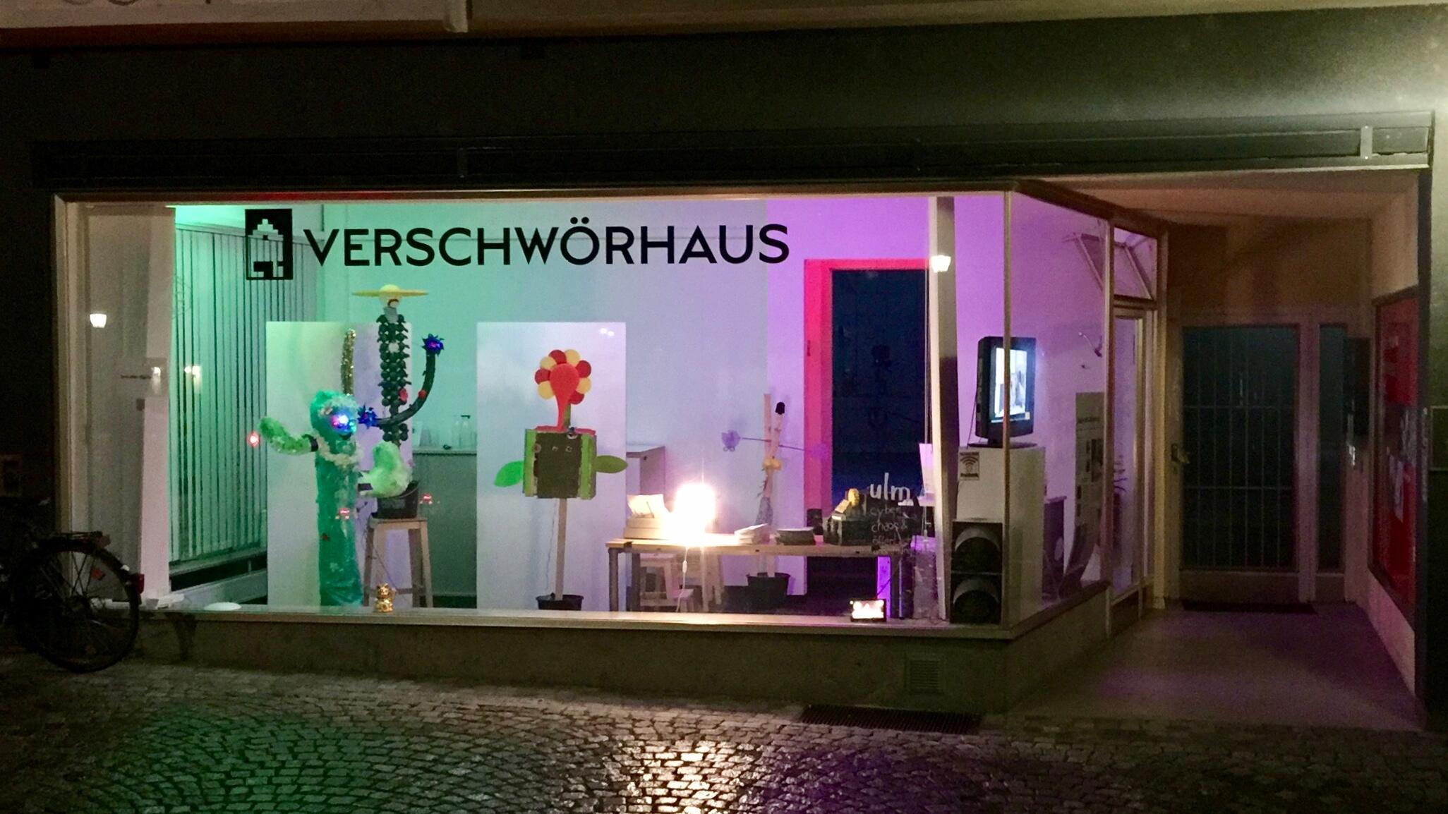 Bunt beleuchtetes Schaufenster mit Aufschrift Verschwörhaus.