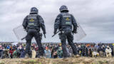 Zwei Polizisten stehen auf einem Damm vor einer demonstrierenden Menschenmenge in Lützerath