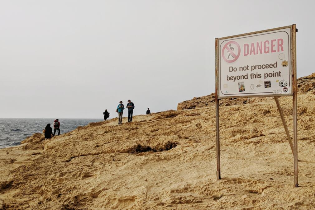 Menschen am Strand im Hintergrund, vorne eine Schild mit der Aufschrift Danger.