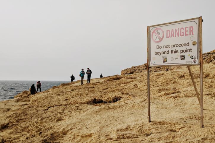 Menschen am Strand im Hintergrund, vorne eine Schild mit der Aufschrift Danger.