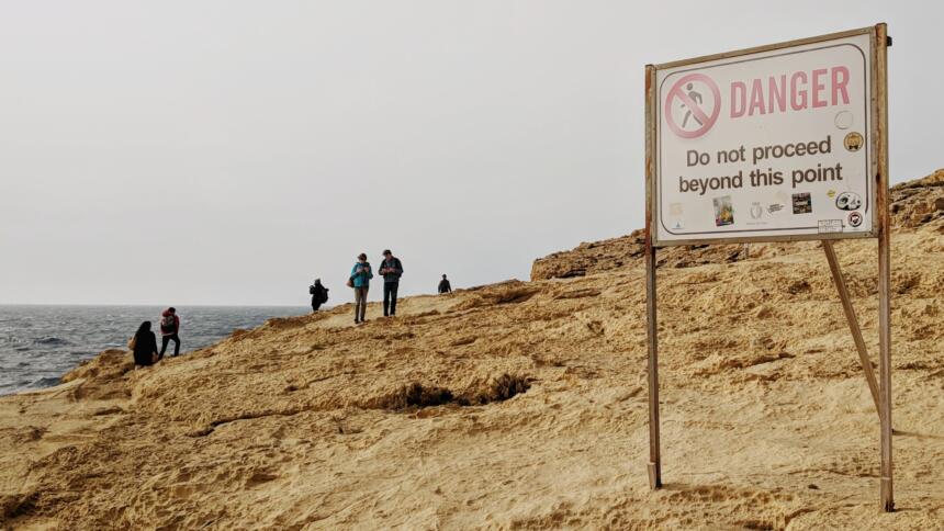 Menschen am Strand im Hintergrund, vorne eine Schild mit der Aufschrift Danger.