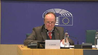 Eric Lefevre sitzt auf einem Podium im Europäischen Parlament und liest den anwesenden Abgeordneten aus einer langen Liste vor.