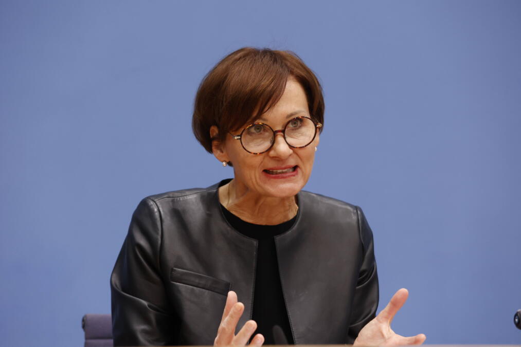 Bundesministerin für Bildung Forschung Bettina Stark-Watzinger mit schwarzer Jacke, kurzen roten Haaren und Briller vor blauem Hintergrund