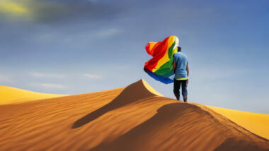 Eine Person steht mit einer Regenbogenflagge auf einer Sanddüne inmitten der Wüste