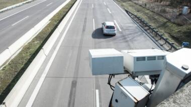 Ein Kennzeichenscanner, der eine Überwachungskamera ähnlich sieht, ist auf die Autobahn gerichtet, auf der man ein Auto sieht.