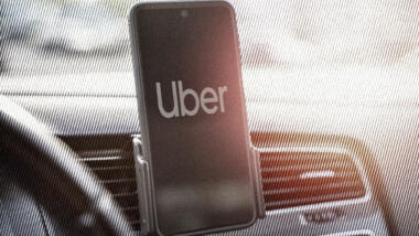 Ein Handy mit der Uber-App klemmt in einer Halterung neben dem Lenkrad.